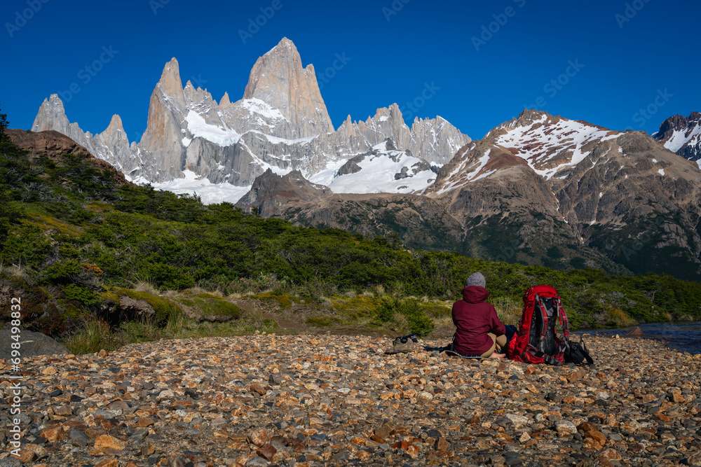 A woman taking a break after long trekking to campsite with beautiful fitzroy, river and clear sky (patagonia, argentina) 