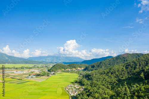 The traditional villages in the middle of the green and yellow rice fields in the valley, Asia, Vietnam, Tonkin, Dien Bien Phu, in summer, on a sunny day. photo