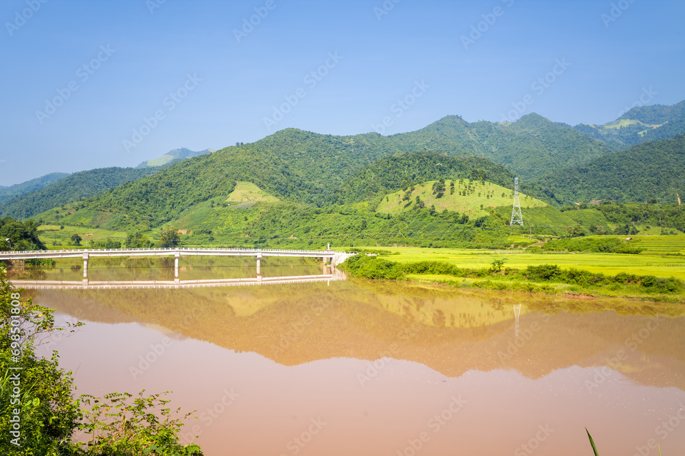 A bridge over a red river in the middle of green mountains, in Asia, Vietnam, Tonkin, between Dien Bien Phu and Lai Chau, in summer, on a sunny day.