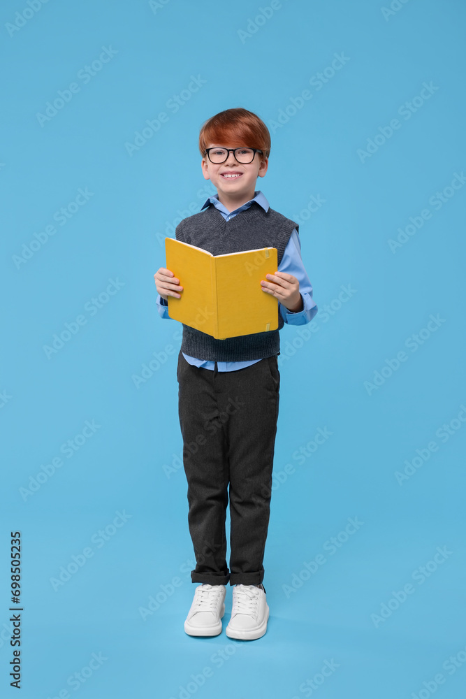 Smiling schoolboy in glasses with book on light blue background Smiling schoolboy in glasses with book on light blue background