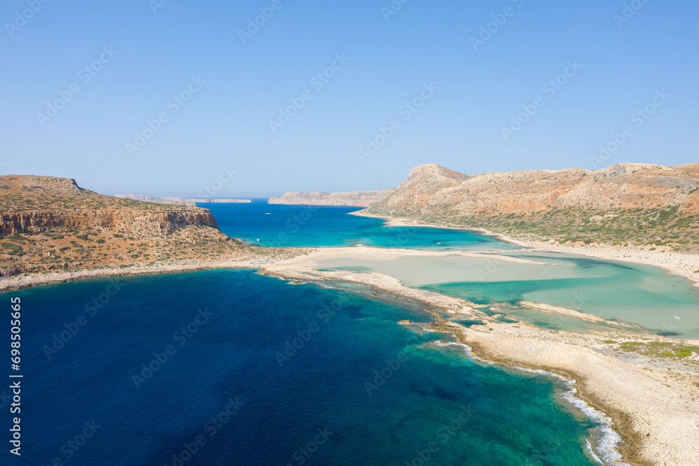 The sandy beach with pink reflections at the foot of the rocky cliffs, in Europe, Greece, Crete, Balos, By the Mediterranean Sea, in summer, on a sunny day. The sandy beach with pink reflections at the foot of the rocky cliffs, in Europe, Greece, Crete, Balos, By the Mediterranean Sea, in summer, on a sunny day.