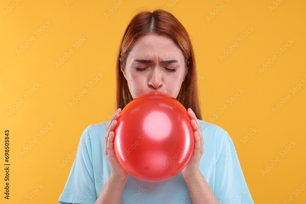 Woman inflating red balloon on orange background Woman inflating red balloon on orange background