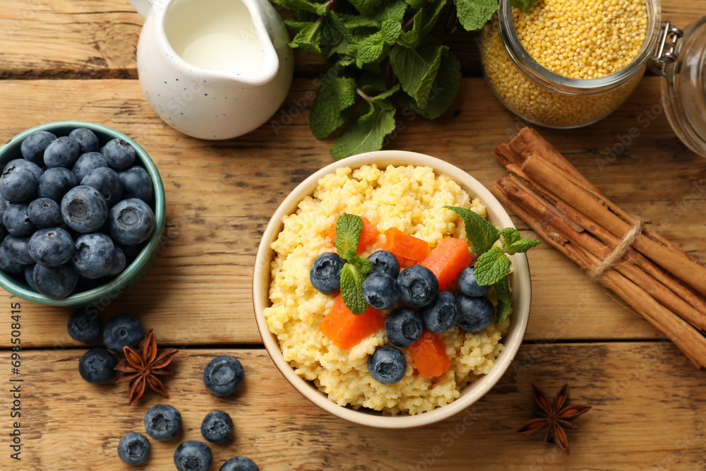 Tasty millet porridge with blueberries, pumpkin and mint in bowl on wooden table, flat lay Tasty millet porridge with blueberries, pumpkin and mint in bowl on wooden table, flat lay
