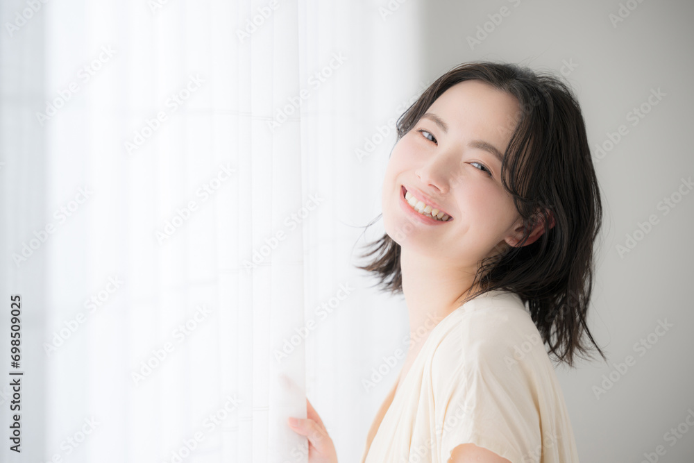 Young woman standing by the window, smiling for the camera Young woman standing by the window, smiling for the camera