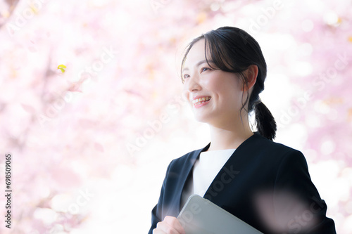 桜の中でパソコンを持つビジネス女性　新卒、新入社員や春の就職のイメージ photo