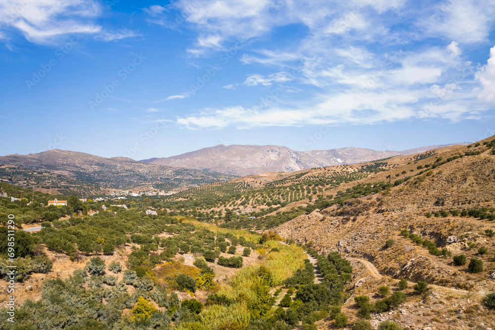 The green countryside at the foot of the rocky mountains , in Europe, Greece, Crete, towards Ierapetra, By the Mediterranean Sea, in summer, on a sunny day.
