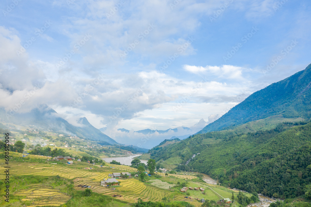 The traditional village with green and yellow rice fields in the green mountains, Asia, Vietnam, Tonkin, Sapa, towards Lao Cai, in summer, on a cloudy day.