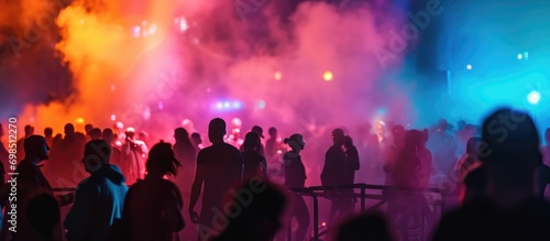 Multicolored lights, smoke, and silhouettes of people on stage create a blurry background for design.