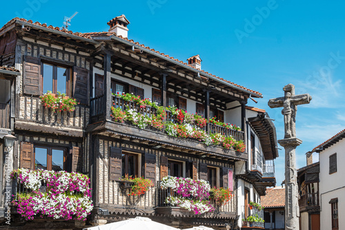 Cruz de piedra del siglo XVIII y hermosa arquitectura tradicional con balcones adornados con macetas y tiestos en la villa medieval de La Alberca, España