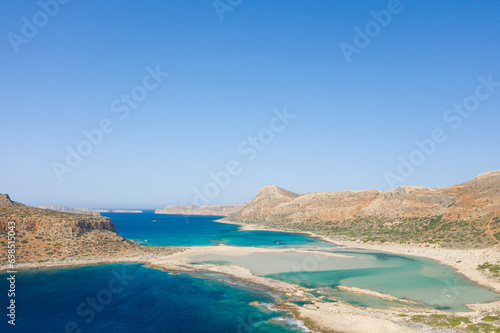 The sandy beach with pink reflections at the foot of the rocky cliffs, in Europe, Greece, Crete, Balos, By the Mediterranean Sea, in summer, on a sunny day. © Florent