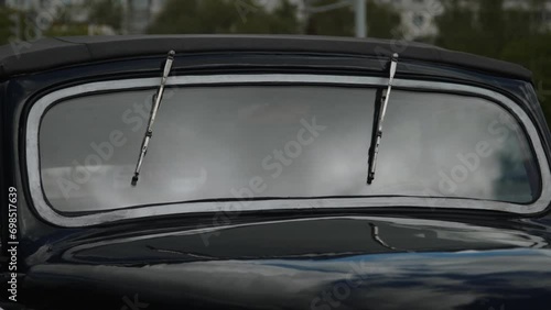 Windshield of old car with windshield wiper blades closeup on street outdoor. Glass of vintage car reflects cloudy sky and shows people passing in city.  photo