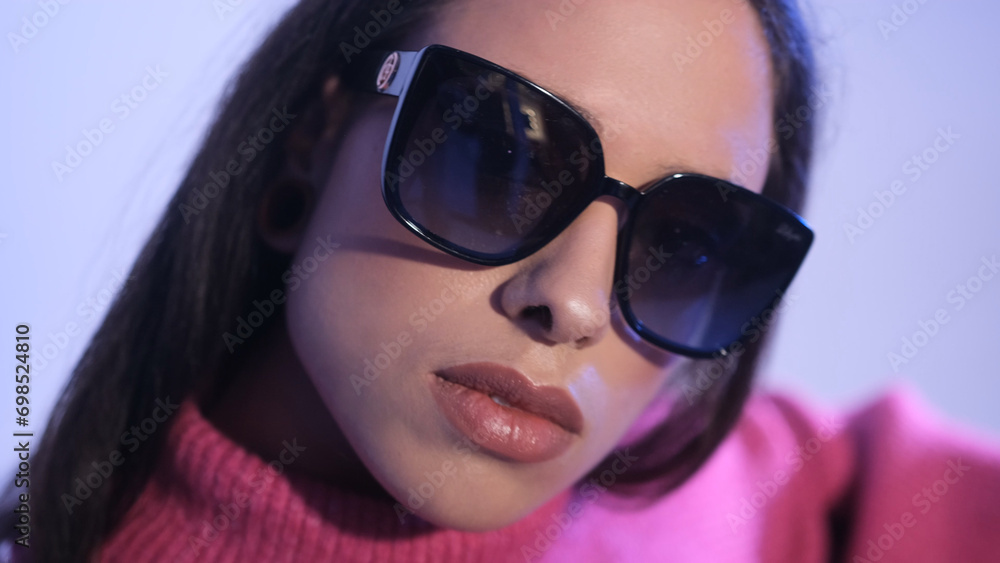A fashionable stylish woman on a blue background in a red sweater and sunglasses poses. A fashionable stylish woman on a blue background in a red sweater and sunglasses poses.