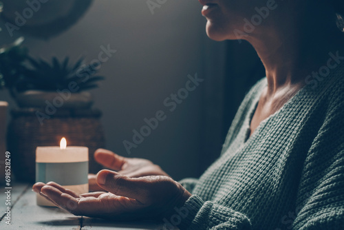 Woman at home in zen meditation activity and candlelight in background. One female people with hands up pray or meditate alone in dark light indoor. Concept of healthy mental lifestyle. Nature