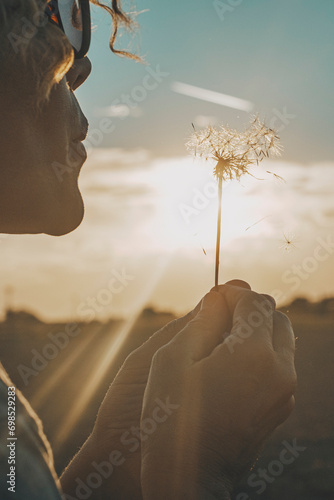 Day dreaming leisure activity with woman blowing a dandelion outdoor in the nature park. Emotion and love lifestyle people concept. Freedom and travel dreams. Sky and sunset in background photo