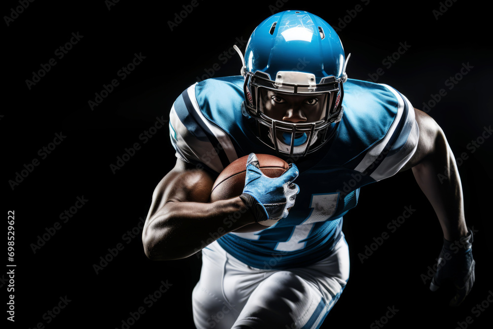 Portrait of American football player running with the ball. Muscular athlete in a blue and white uniform with an ovoid ball in a dynamic pose. Isolated on black background. Portrait of American football player running with the ball. Muscular athlete in a blue and white uniform with an ovoid ball in a dynamic pose. Isolated on black background.