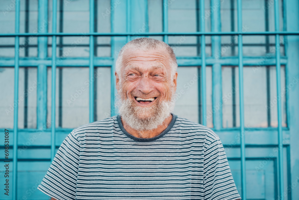 75 year old senior man laughs while having a good time outdoors. Portrait with blue background. Leisure and people concept 75 year old senior man laughs while having a good time outdoors. Portrait with blue background. Leisure and people concept