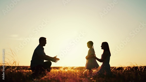 Father mother and daughter revelled in joy of evening in meadow surrounded by wheat field. Sun sends rays on daughter after hugging with mother and running to father embrace. Sun dipped below horizon