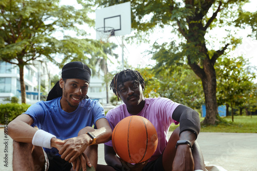 Cheerful Black men resting after playing streetball together after work