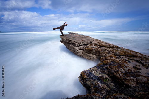 A daring businessman walks a fine line  from a rock to the sea. 