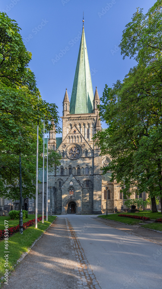 Vertical photo featuring an alley through a park leading to the main entrance of Nidaros Cathedral in Trondheim