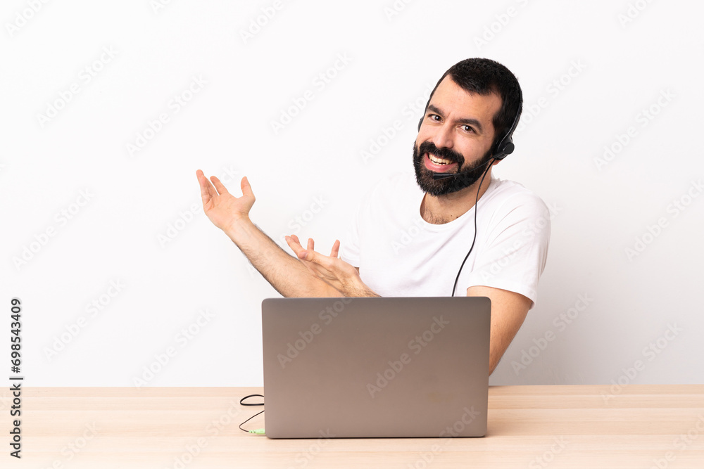Telemarketer caucasian man working with a headset and with laptop extending hands to the side for inviting to come. Telemarketer caucasian man working with a headset and with laptop extending hands to the side for inviting to come.