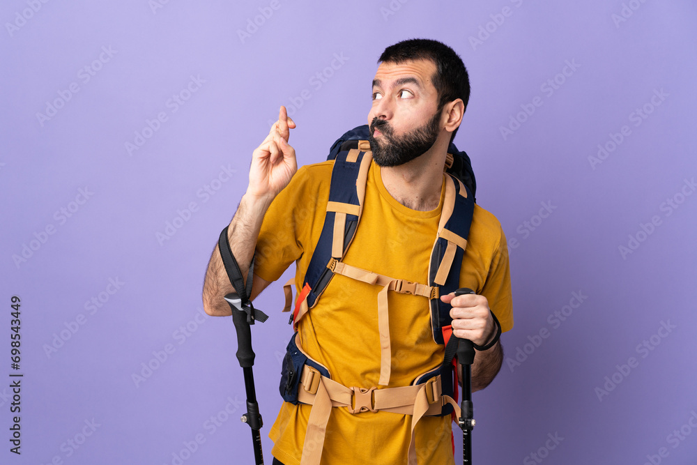 Caucasian handsome man with backpack and trekking poles over isolated background with fingers crossing and wishing the best Caucasian handsome man with backpack and trekking poles over isolated background with fingers crossing and wishing the best
