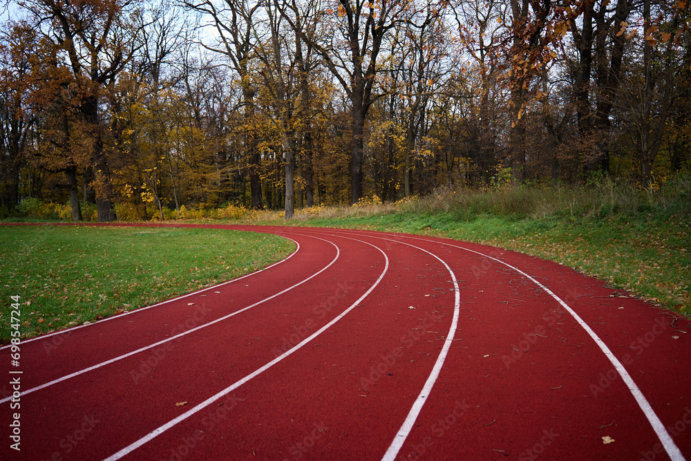 Obraz premium Red runninng race track with lanes at autumn park, Treadmill at stadium, Sport and fitness concept