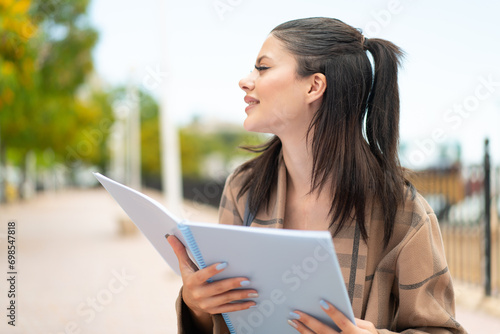 Young pretty woman at outdoors holding a notebook