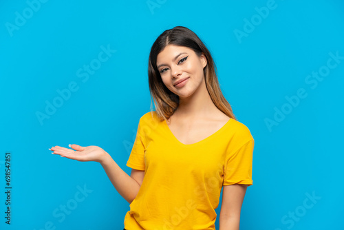 Young Russian girl isolated on blue background presenting an idea while looking smiling towards