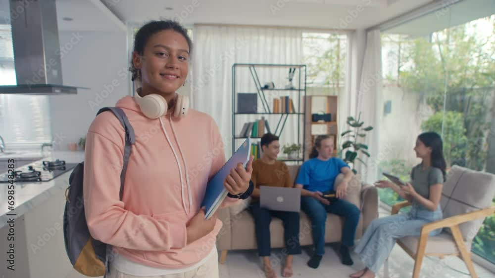 Portrait of teenage girl holding educational materials while preparing for exam with friends at home, looking at camera Portrait of teenage girl holding educational materials while preparing for exam with friends at home, looking at camera