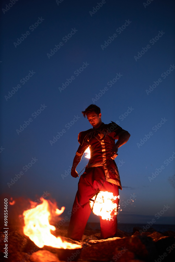 Vertical portrait of young male performer juggling fire poi outdoors at night