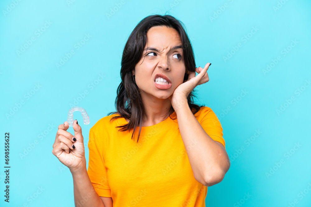 Young hispanic woman holding invisible braces isolated on blue background frustrated and covering ears Young hispanic woman holding invisible braces isolated on blue background frustrated and covering ears