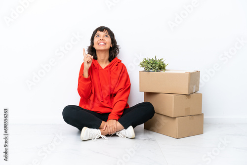 Young girl moving in new home among boxes isolated on white background pointing up and surprised