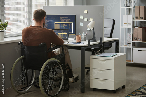 Back view of adult man with disability as computer programmer writing code at workplace in office, copy space