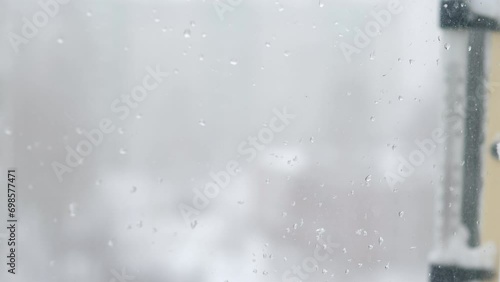 snowfall outside the window, snow-covered thermometer outside on a winter day. snowflakes fall on the window glass. snow storm outside the window photo