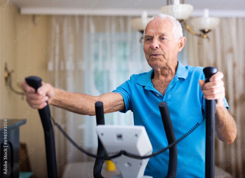 Elderly man exercising on elliptic trainer in living room Elderly man exercising on elliptic trainer in living room