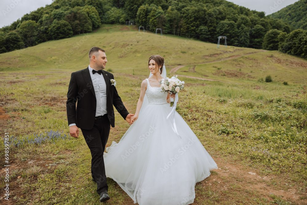 Portrait of a young bride and groom walking on green grass in a large field after the wedding ceremony, front view. Happy wedding couple, copy space
