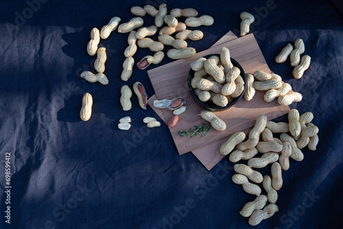 Top down view on a peanuts in a shell laying in a group on a blue fabric table cloth. Some peanuts are peeled.