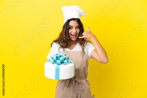 Young caucasian pastry chef woman with a big cake isolated on yellow background making phone gesture. Call me back sign