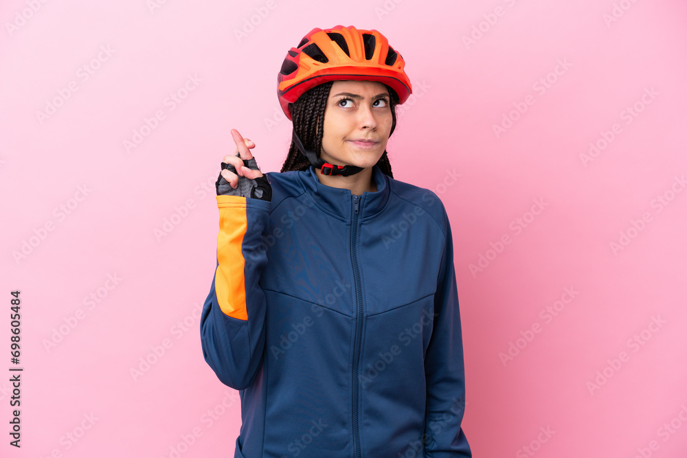 Teenager cyclist girl isolated on pink background with fingers crossing and wishing the best - obrazy, fototapety, plakaty 