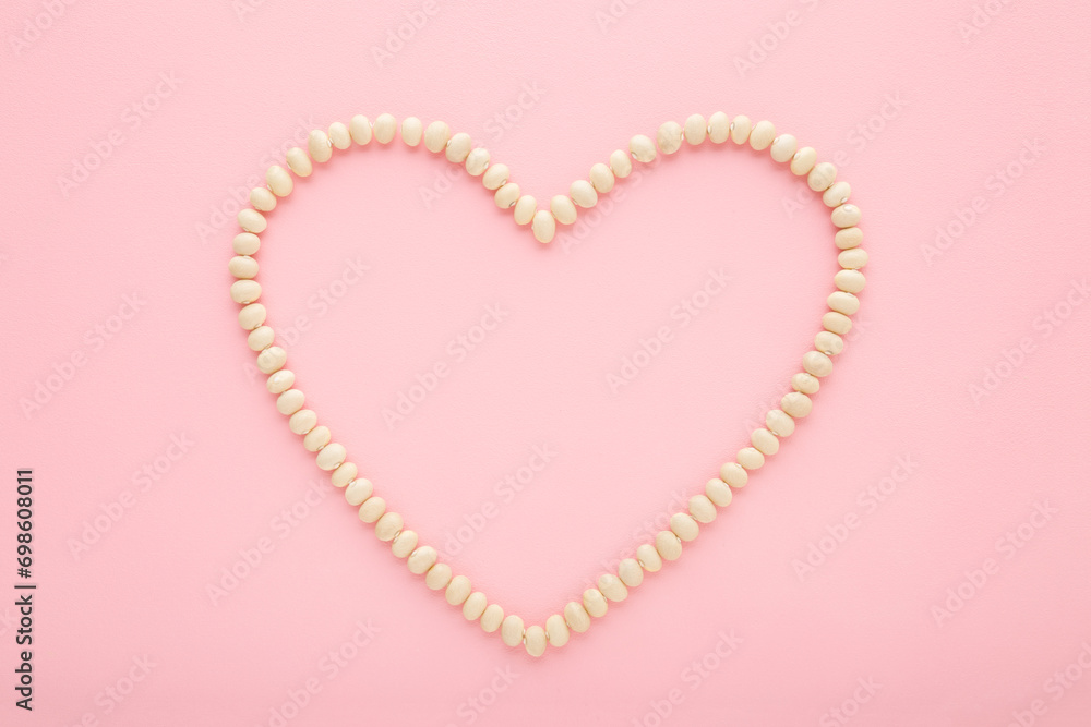 Heart shape created from fresh dry white beans on light pink table background. Pastel color. Love healthy food. Closeup. Top down view. Empty place for text.