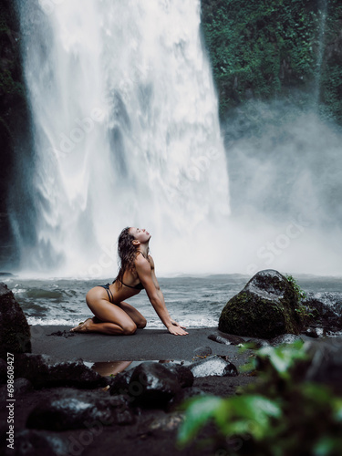 Woman in swimsuit posing near powerful waterfall. Traveler girl on waterfall in Bali