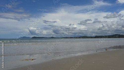 Ocean waves roll towards the shore and spread over the beach. Clouds and blue sky are reflected on the smooth wet sand. Tropical islands in the distance. Malaysia. Borneo. Kota Kinabalu