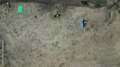 construction work begins with an archaeological survey. a truck is importing topsoil. archaeologists dig up buckets of finds. A wheelbarrow takes the loess out of the pit. ladder inside, covered with  photo