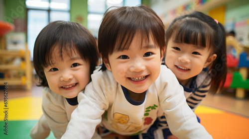 日本の幼稚園児・保育園児3人が長袖の私服でカメラに向かってきて笑っている写真、背景教室、保育室