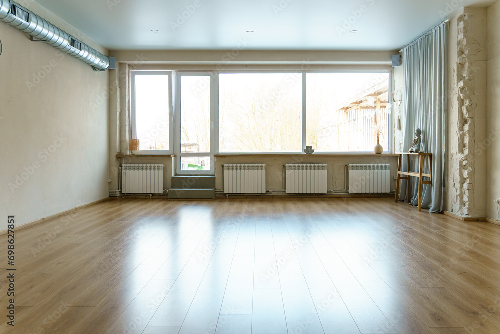 Fototapeta premium A spacious empty hall with columns and large windows. A gym with wooden floors for yoga and fitness classes. Interior design of the fitness center. A large room without furniture.