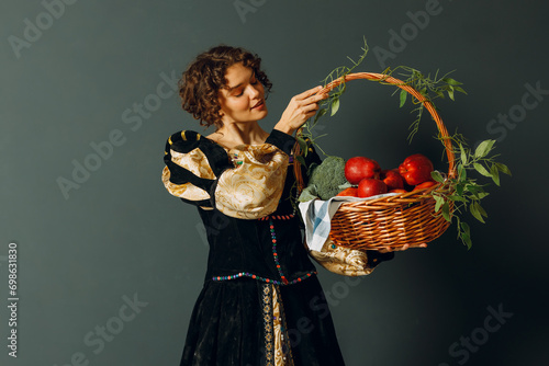 Portrait of a young adult woman dressed in a medieval dress holding a basket with vegetables and fruits in her hands photo