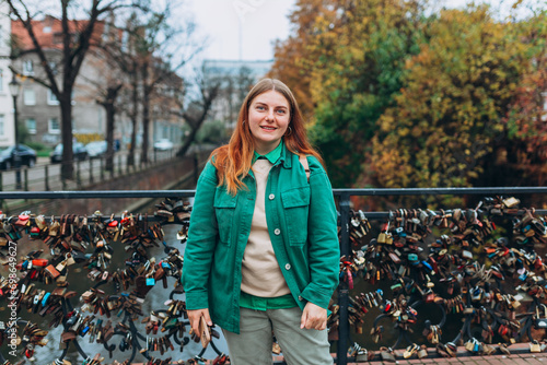 Happy cheerful young woman with backpack walking on city street checks her smartphone. Portrait of beautiful 30s girl using smartphone outdoors. Urban lifestyle concept. photo