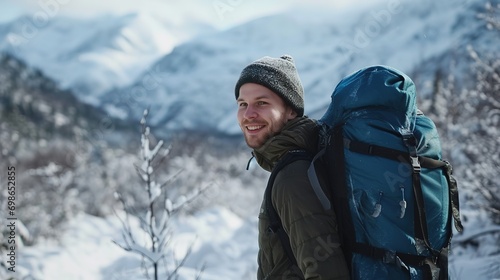 smiling man look at the camera with a big blue backpack, on his shoulders walking through the winter mountains