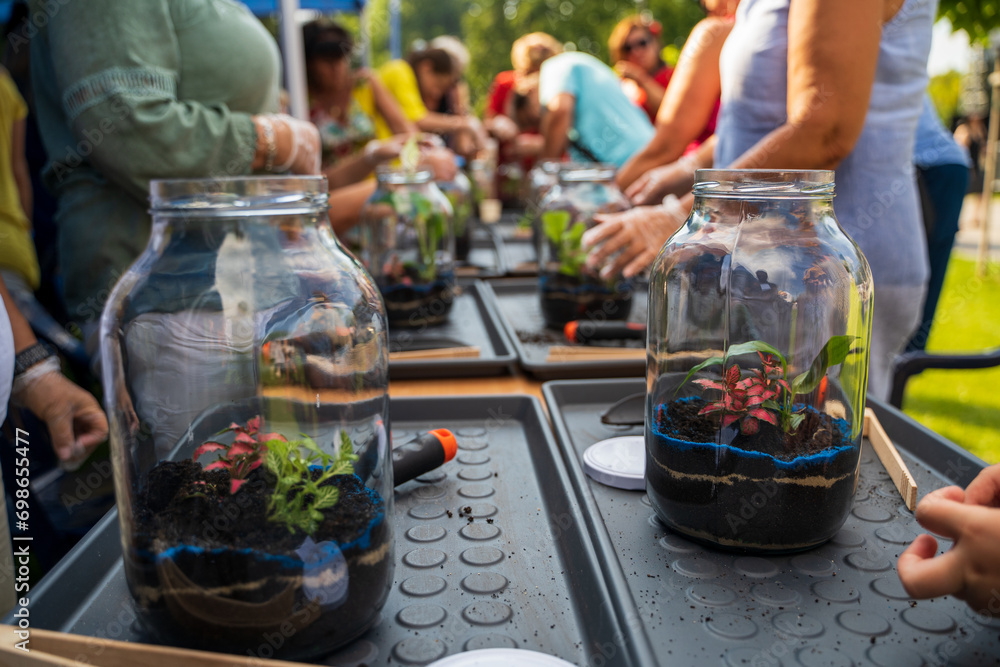 Bunch of people gathered together for environment on a workshop to plant seed in miniature glass jar with soil inside. Selective focus and small depth of field